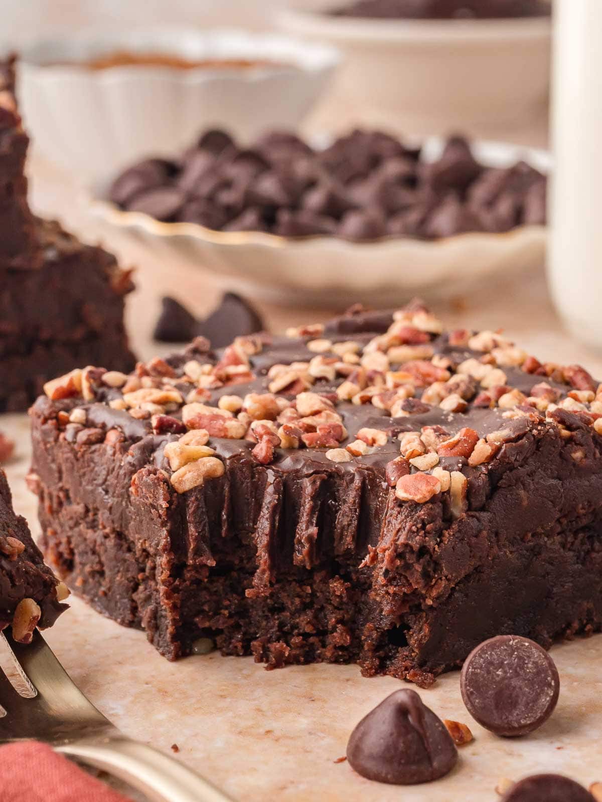 Fudgy Texas Sheet Cake square topped with chopped pecans, showing a soft brownie like center and thick chocolate frosting with a bite taken out.