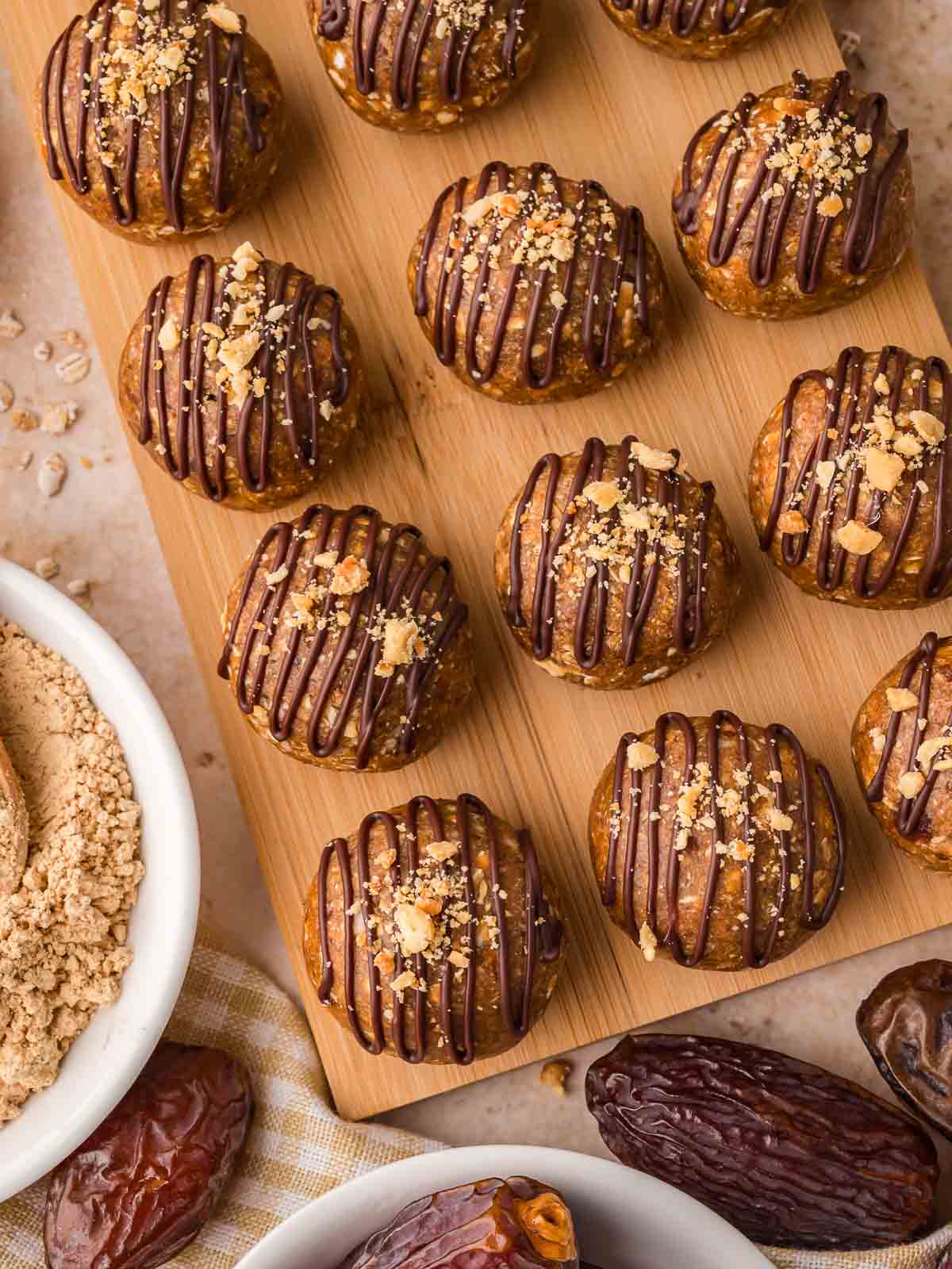 Overhead view of peanut butter protein balls arranged on a board with dates, oats, and PB2 in bowls around them.