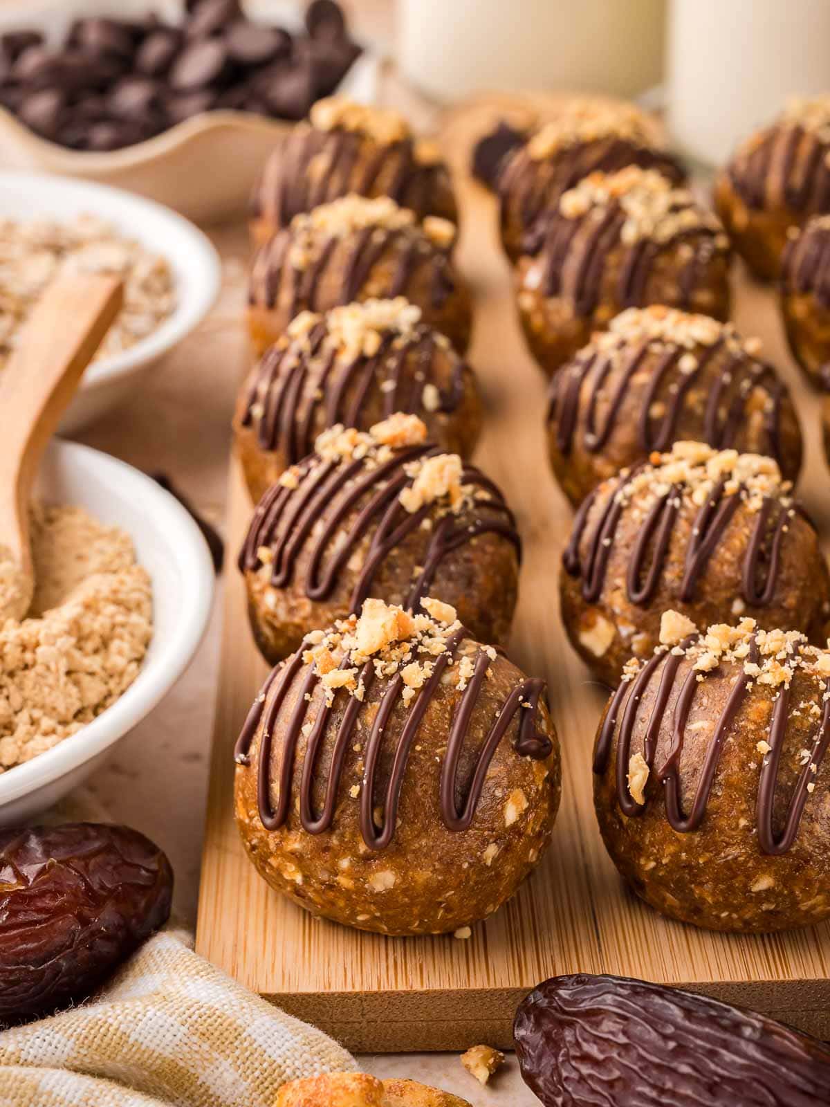 Peanut butter protein balls lined up on a wooden board with chocolate drizzle and chopped peanuts on top.