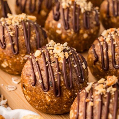 Rows of peanut butter protein balls drizzled with chocolate and sprinkled with crushed peanuts.