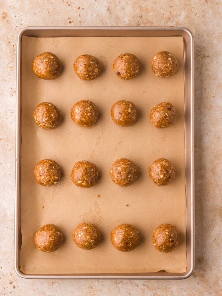 Rolled peanut butter protein balls lined up on a parchment-covered baking sheet before chilling.