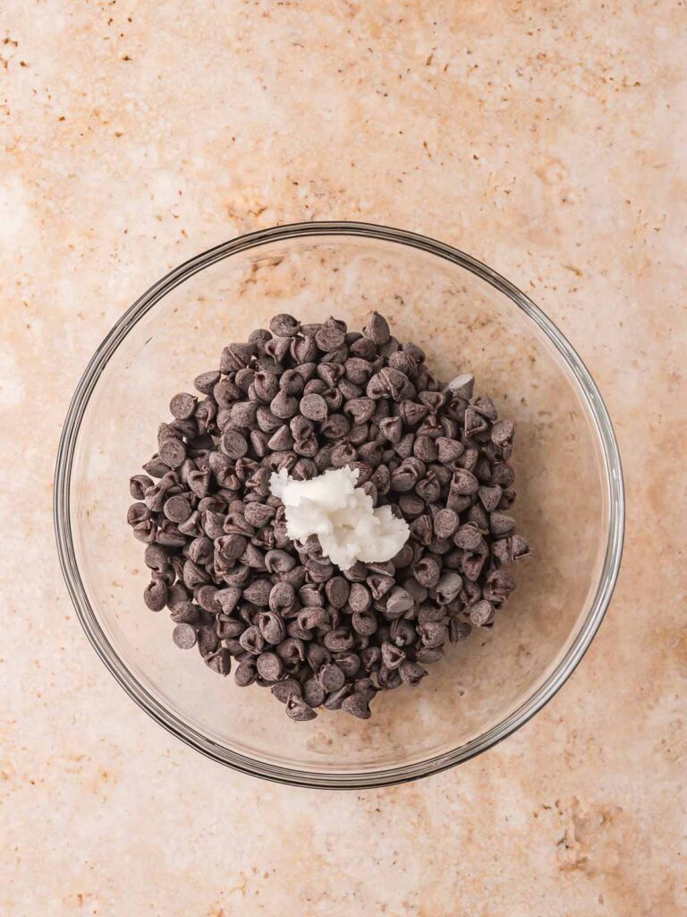 Bowl of Lily’s chocolate chips with a spoonful of coconut oil ready to melt for drizzling over protein balls.