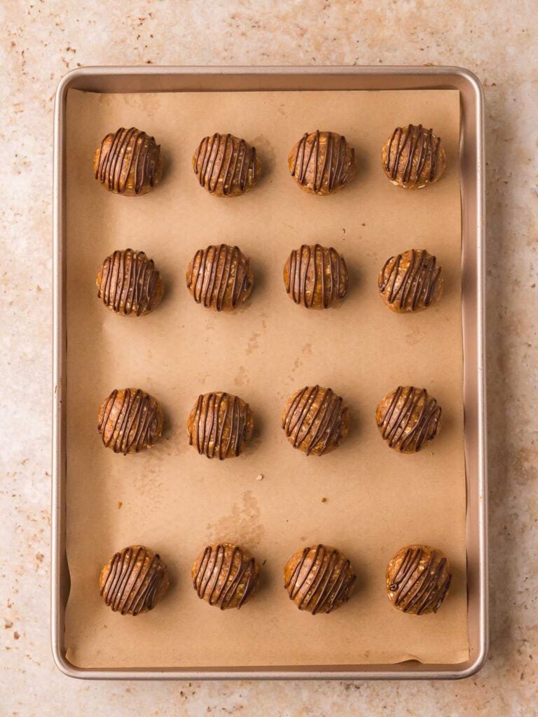 Peanut butter protein balls drizzled with melted chocolate after chilling.