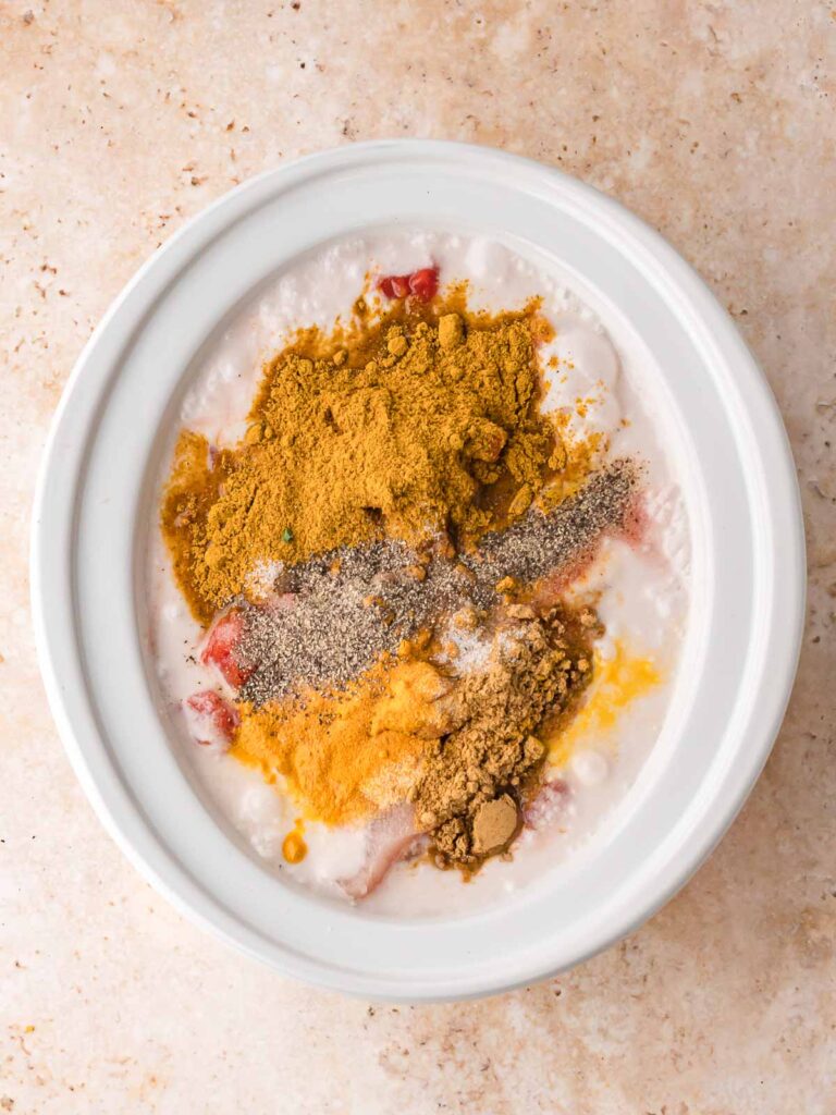 Chicken, diced tomatoes, coconut milk, and curry spices layered in the slow cooker before stirring.