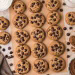 Brown butter chocolate chip cookies arranged on parchment with baking ingredients and chocolate chips nearby.