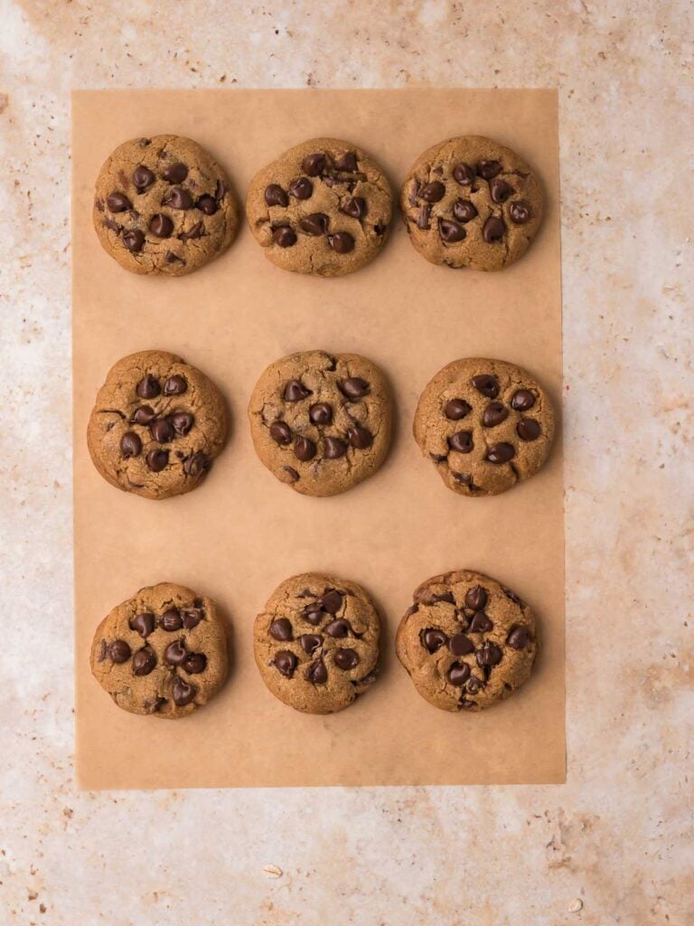 Baked brown butter chocolate chip cookies cooling on parchment paper with chocolate chips on top.