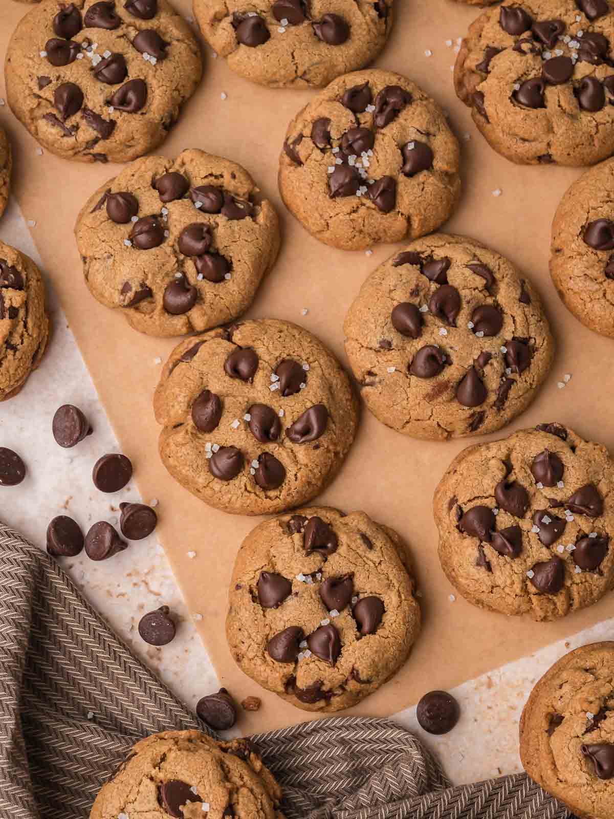 Overhead view of baked brown butter chocolate chip cookies on parchment paper with chocolate chips and sea salt.