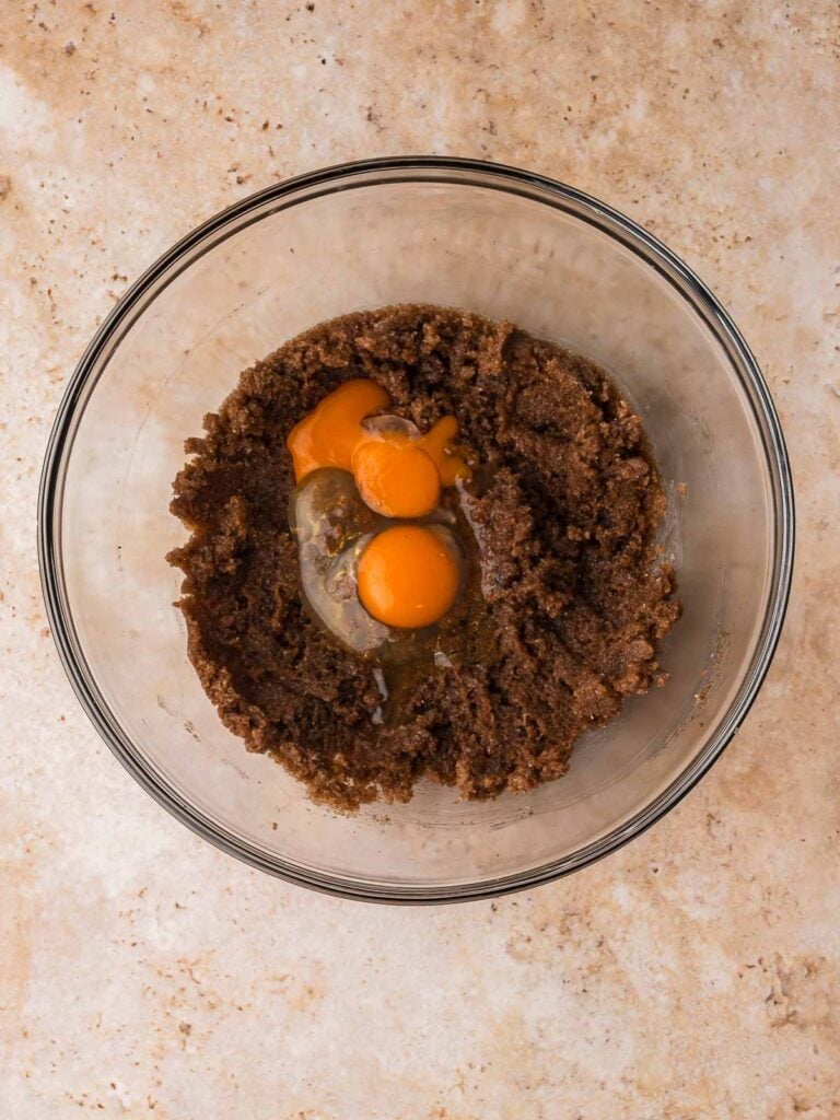 Egg and egg yolk added to the brown butter and sugar mixture in a glass bowl.