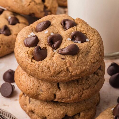 Stack of soft brown butter chocolate chip cookies with chocolate chips and milk in the background.
