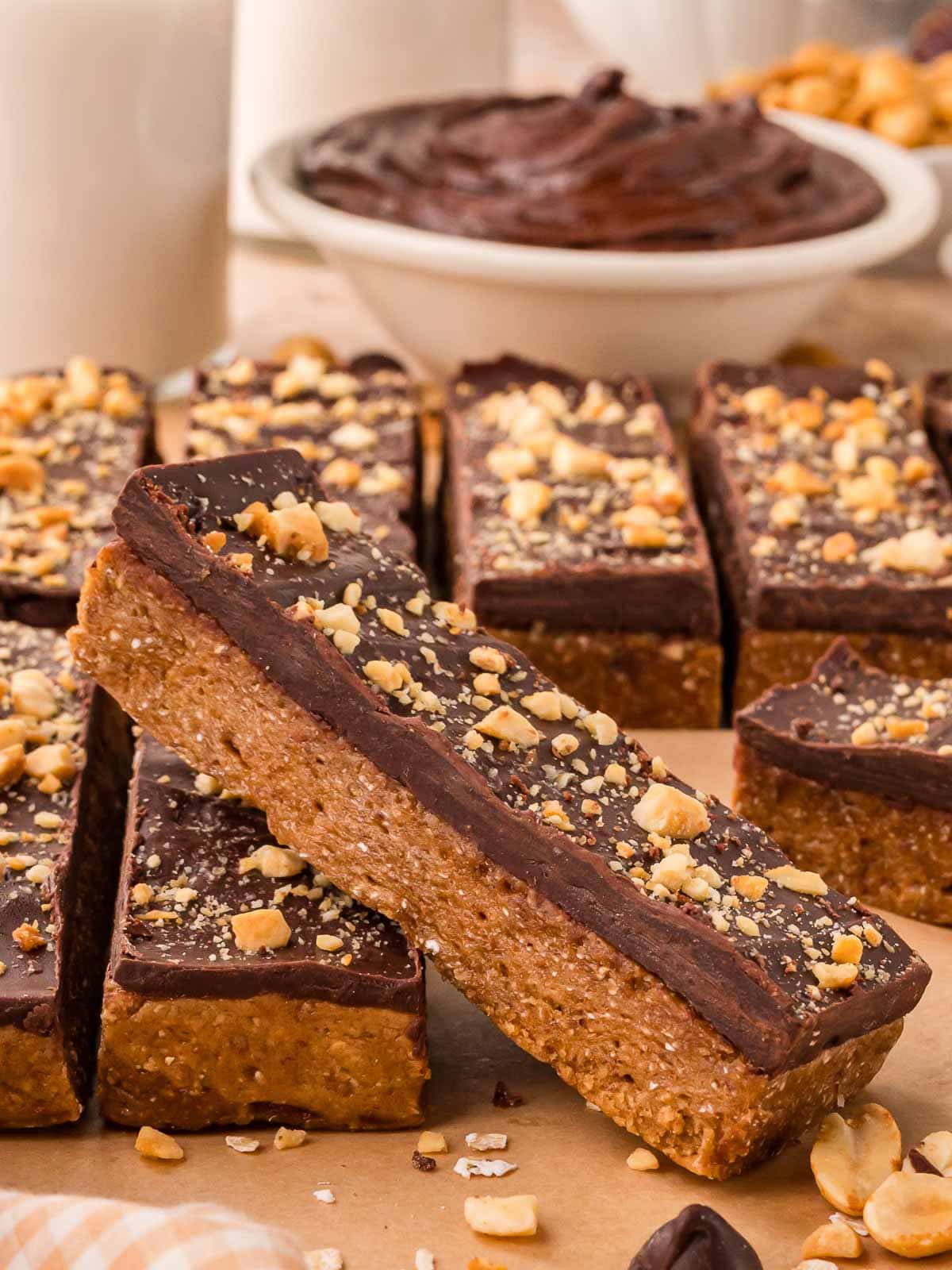 Close-up of chocolate peanut butter protein bars arranged on parchment with chopped peanuts sprinkled over the top.