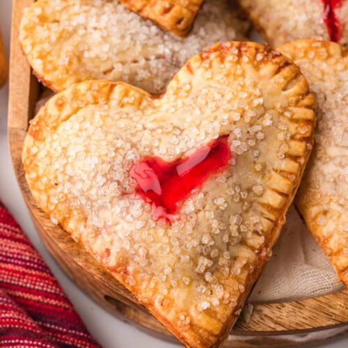 Heart shaped cherry hand pies with crimped edges and cherry filling, arranged on a wooden board.