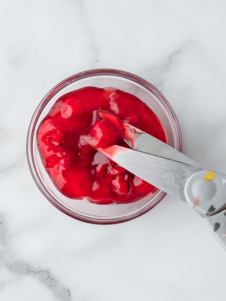 Bowl of cherry pie filling being stirred with a spoon, ready to use for hand pies.