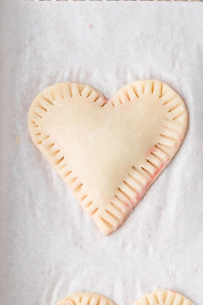 Top pie dough hearts placed over the cherry filling and edges sealed with a fork to form heart-shaped hand pies