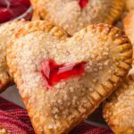 Heart shaped cherry hand pies baked until golden and topped with coarse sugar, shown stacked on a plate.