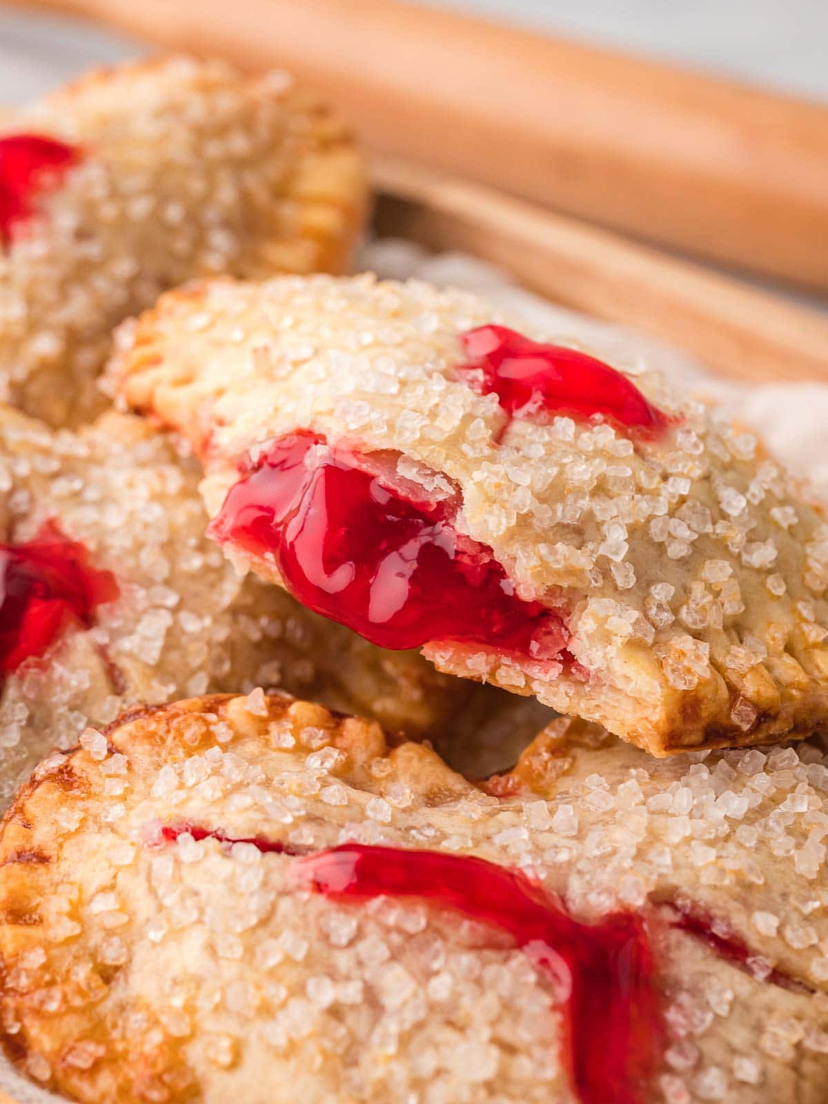 Heart shaped cherry hand pie with flaky pie crust, coarse sugar topping, and cherry pie filling visible in the center.