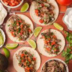 Slow cooker shredded beef tacos on flour tortillas topped with fresh tomato salsa and cilantro.