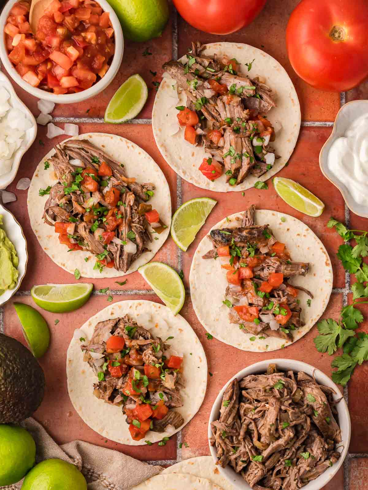 Slow cooker shredded beef tacos on flour tortillas topped with fresh tomato salsa and cilantro.