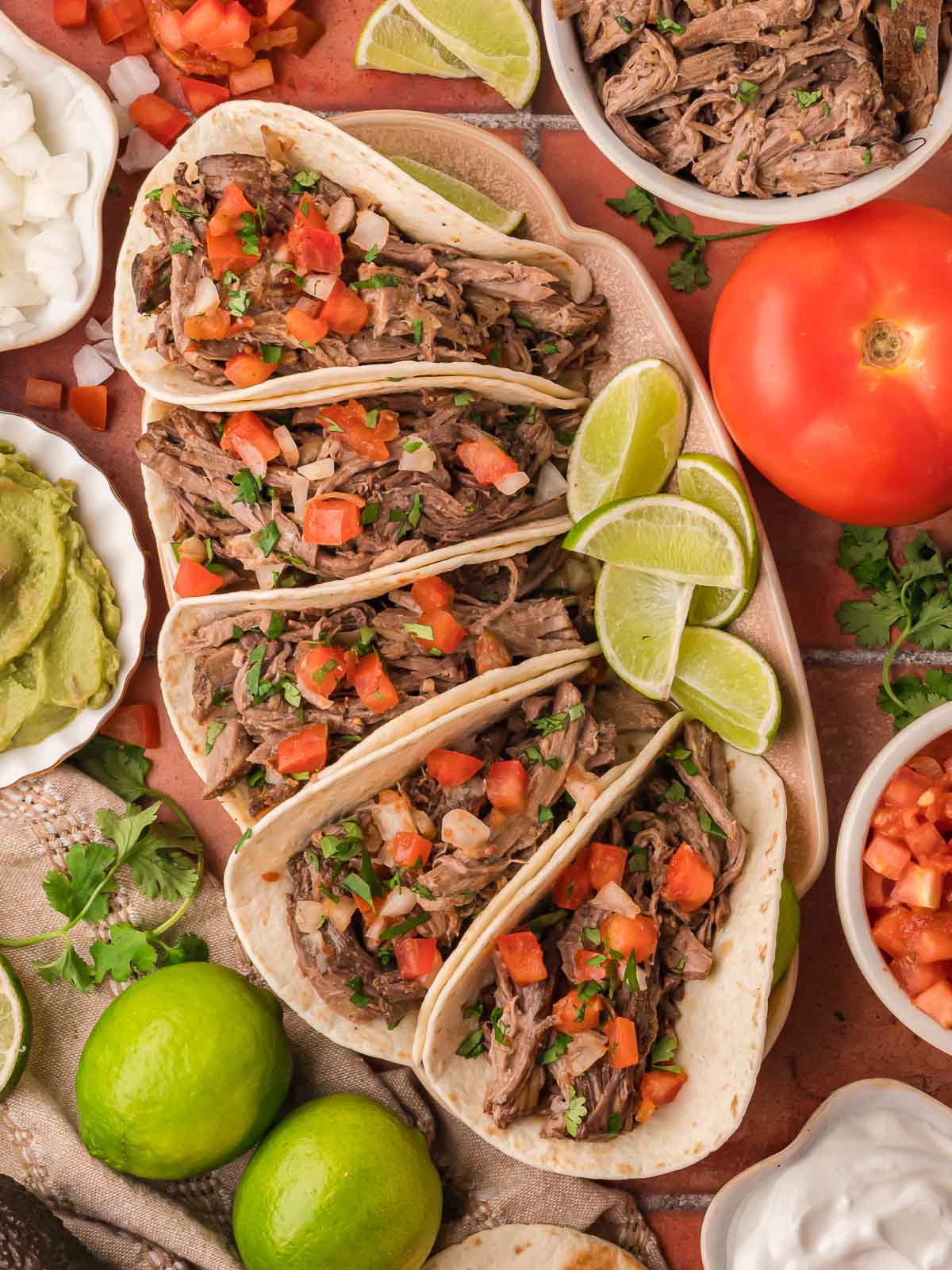 Shredded beef tacos arranged on a platter with fresh salsa, lime wedges, and cilantro.
