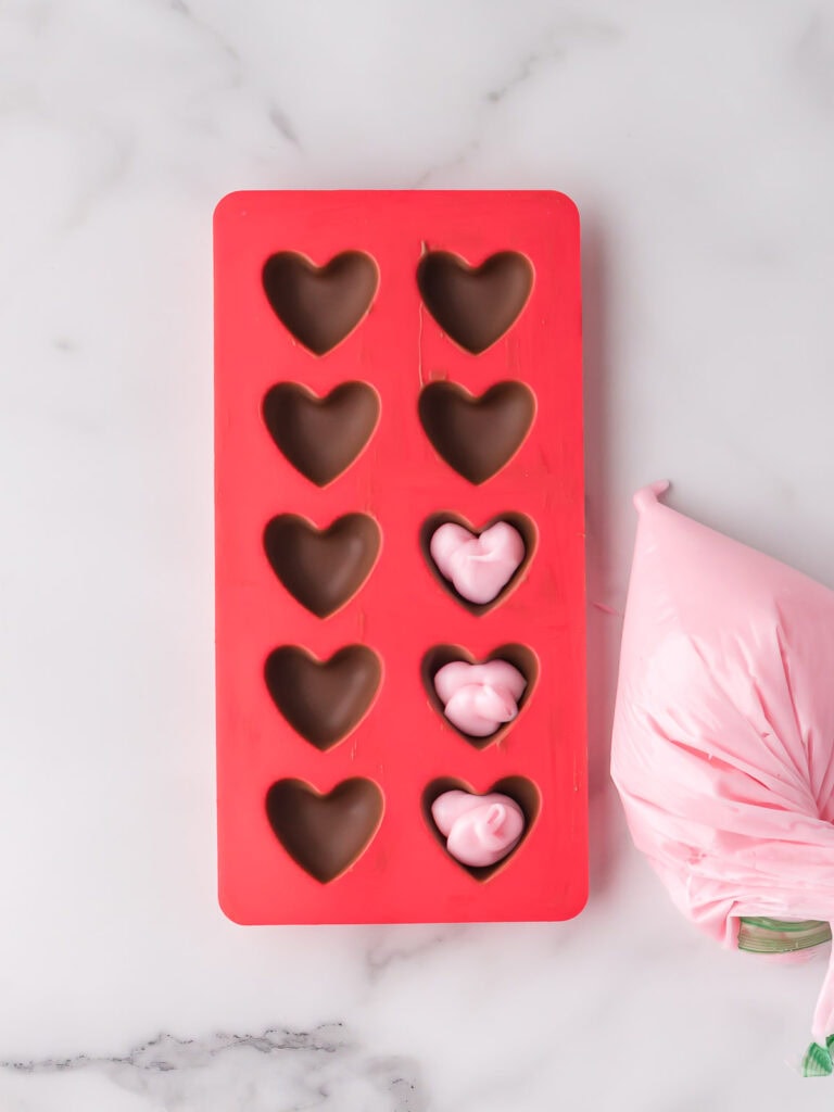 Pink fondant filling transferred to a piping bag and fondant filling piped into heart-shaped chocolate shells.


