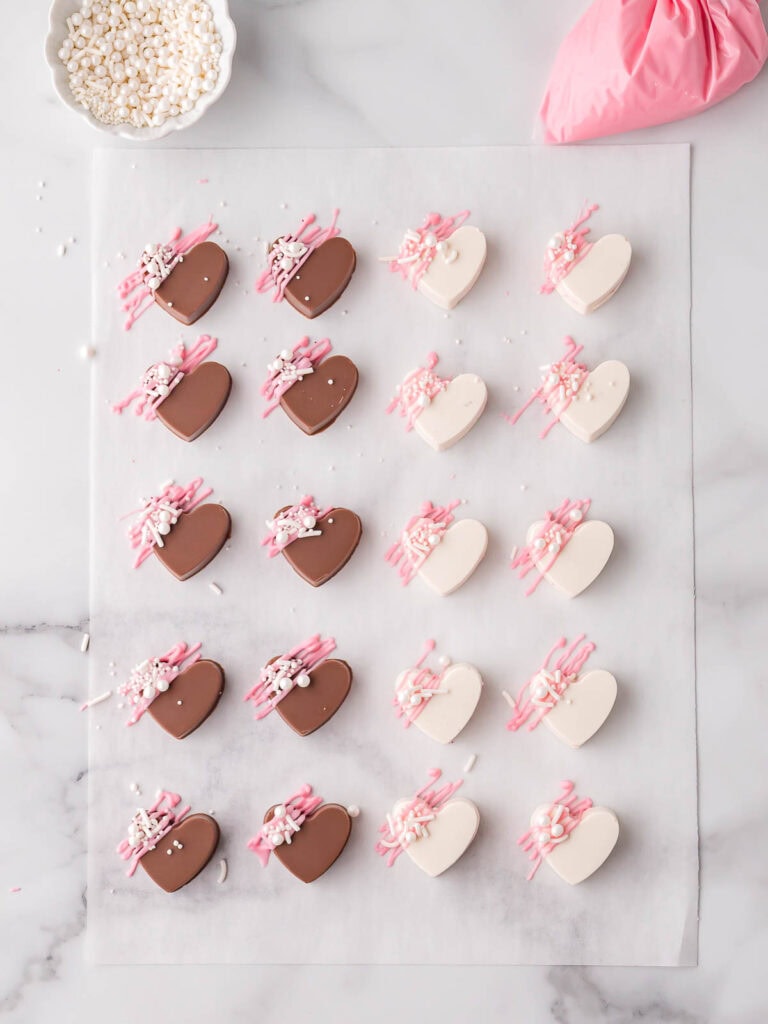 Homemade filled chocolate hearts decorated with pink chocolate drizzle and sprinkles.