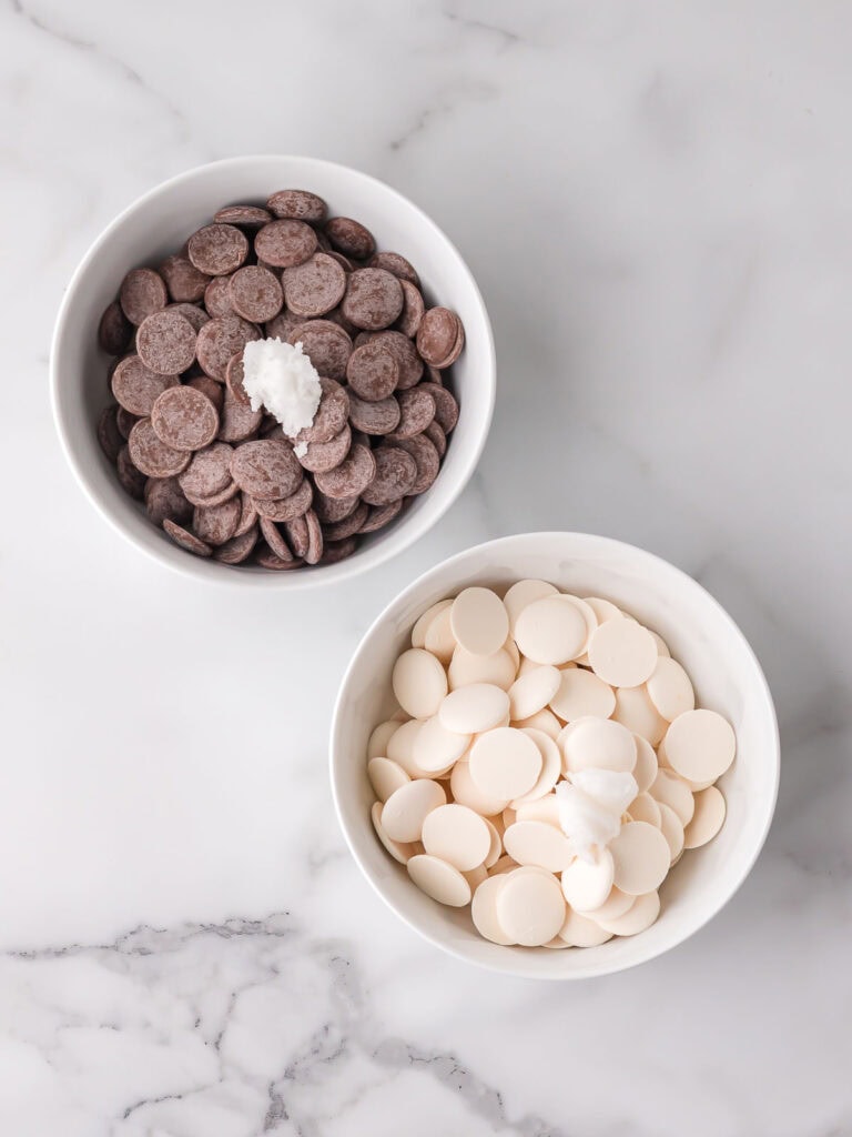 Milk chocolate and white chocolate candy melts in bowls with coconut oil for making homemade filled chocolates.

