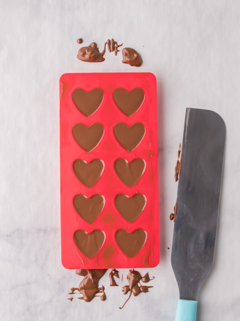 Heart-shaped chocolate molds filled with melted milk chocolate for Valentine’s Day chocolates.

