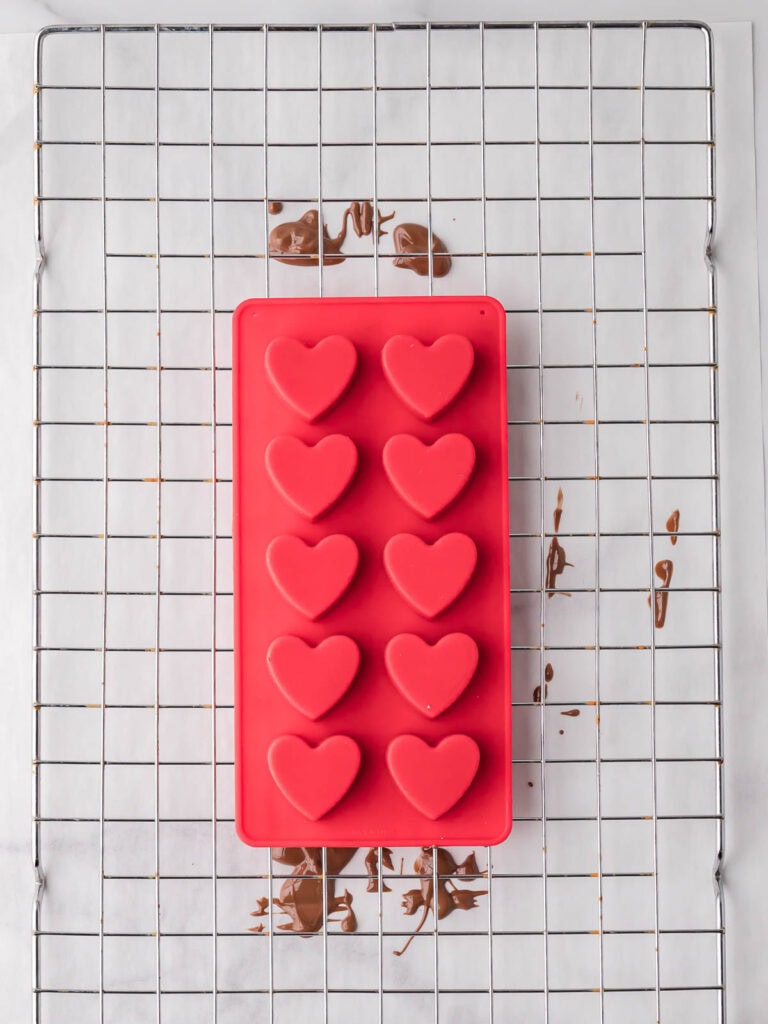 Silicone heart mold flipped upside down over a wire rack to drain excess chocolate.

