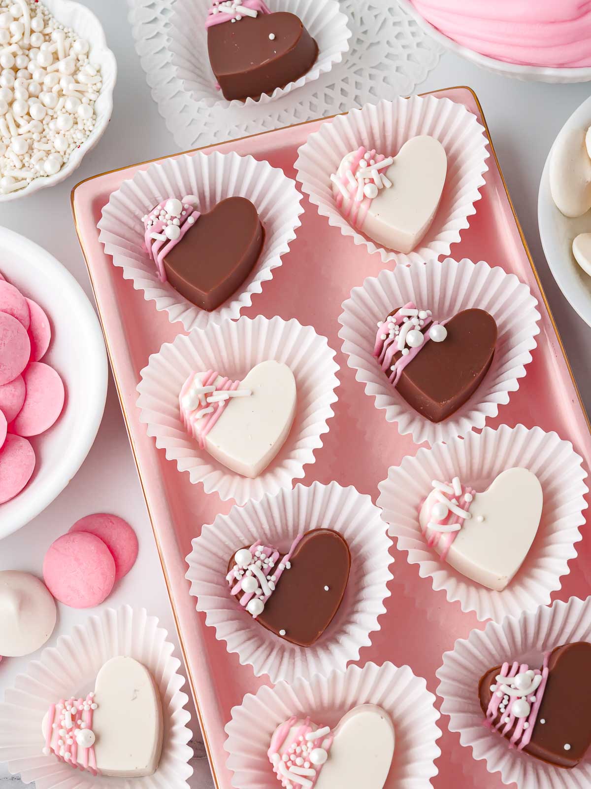 Valentine’s Day chocolate hearts displayed in white candy cups on a pink serving tray.