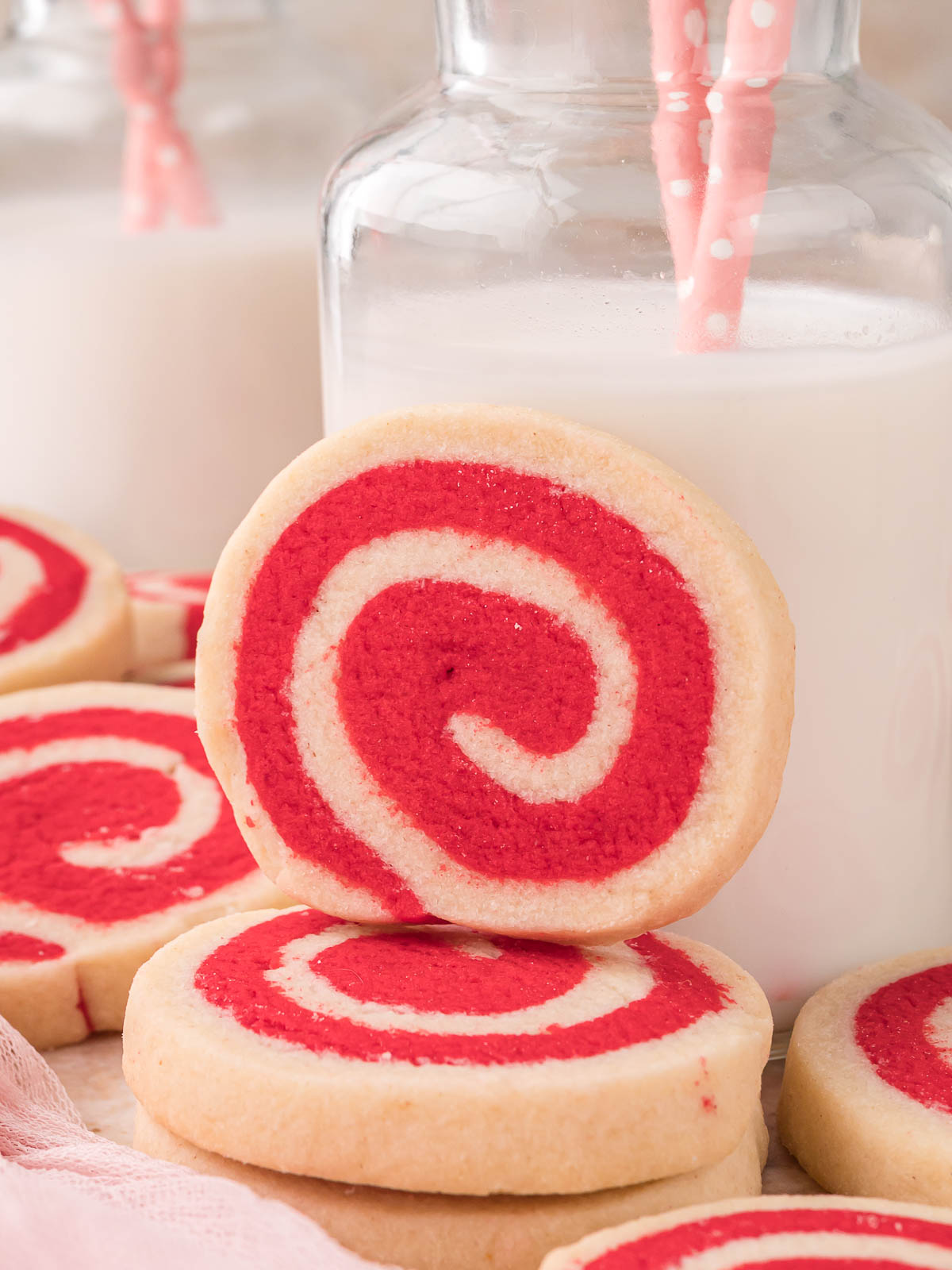 Red and white pinwheel cookies stacked with a glass bottle of milk in the background.