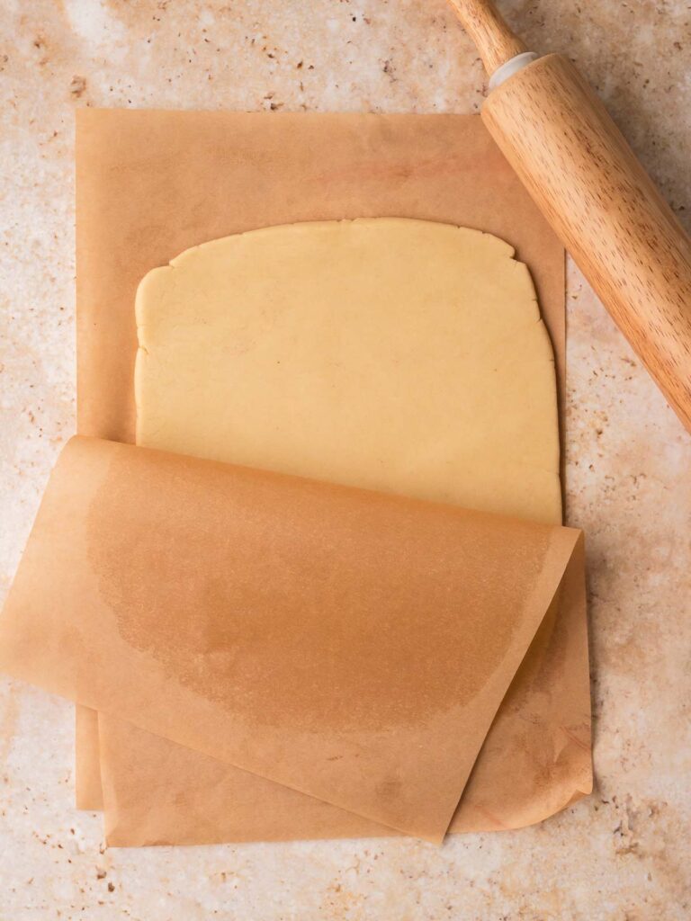 Plain pinwheel cookie dough rolled between parchment paper with rolling pin.