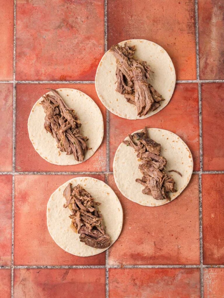 Shredded beef placed onto warmed tortillas for tacos.