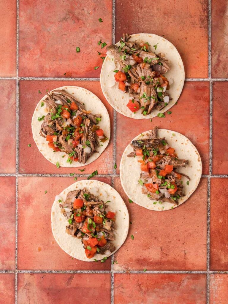 Assembled shredded beef tacos topped with fresh tomato salsa and cilantro.