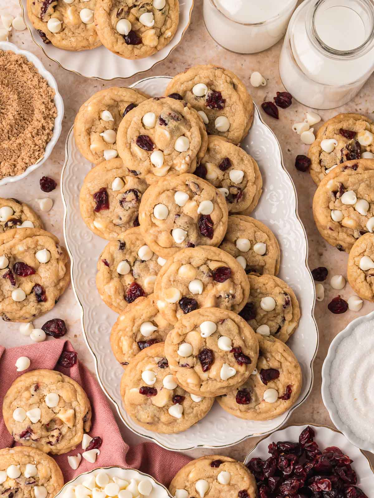 White chocolate cranberry cookies stacked on a serving platter with white chocolate chips and dried cranberries.