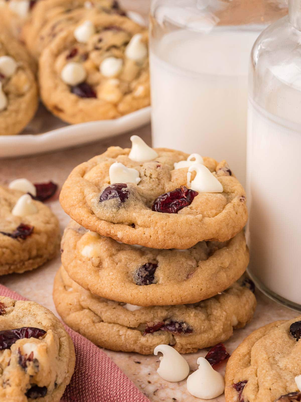 Stack of white chocolate cranberry cookies next to a glass jar of milk.