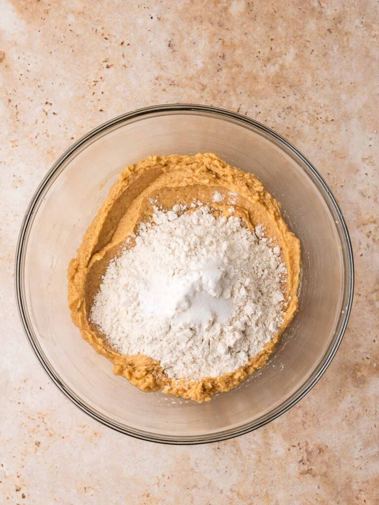 Flour, baking soda, and salt added to cookie dough in a mixing bowl.