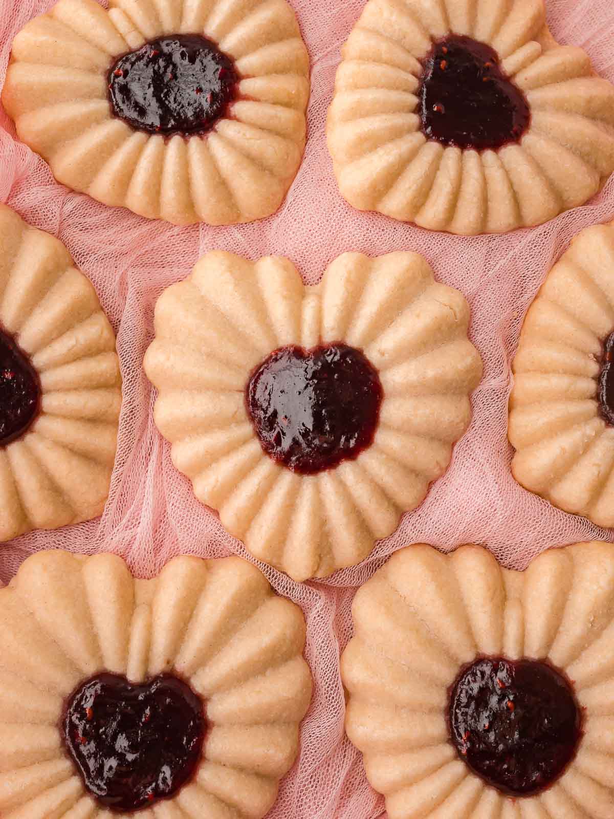 Heart jam cookies arranged on pink fabric with visible jam-filled centers.