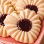 Heart jam cookies stacked on a pink plate with detailed stamped edges.