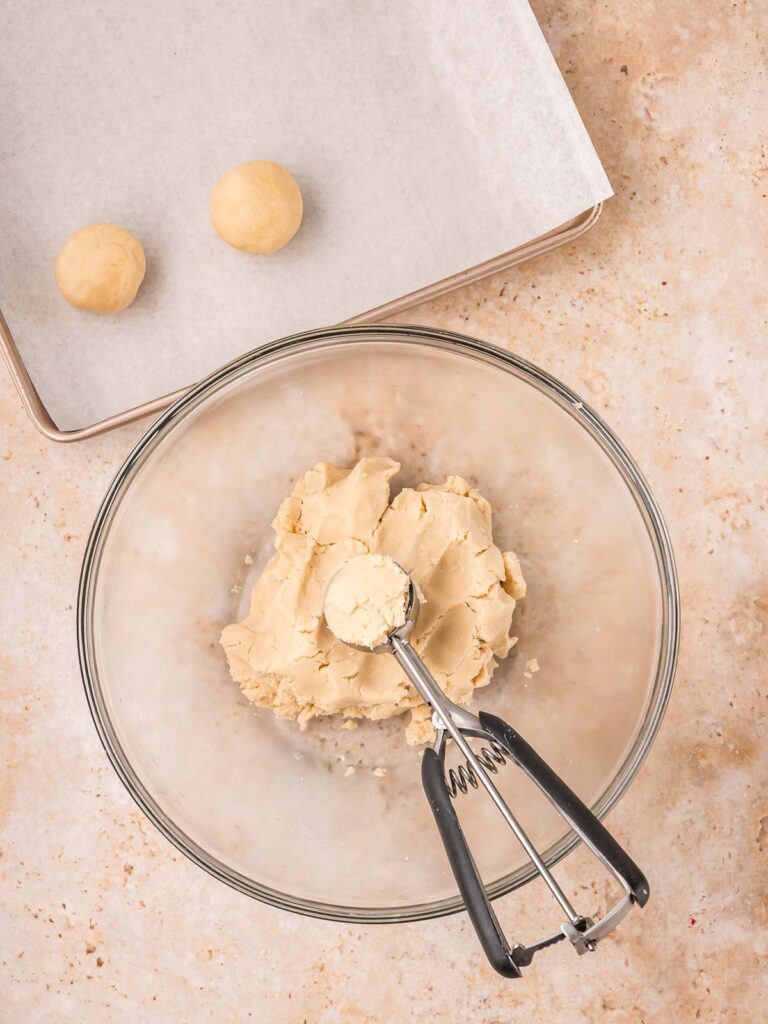 Cookie dough scooped and rolled into evenly sized balls on a parchment-lined baking sheet.