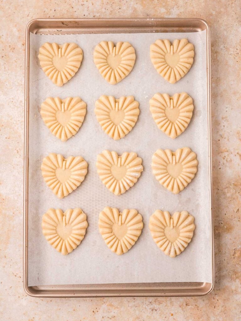 Shaped heart cookies resting on the counter next to the wooden stamp.