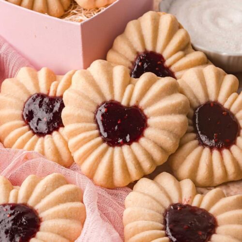 Heart jam cookies displayed together with a pink box and small bowl of jam nearby.