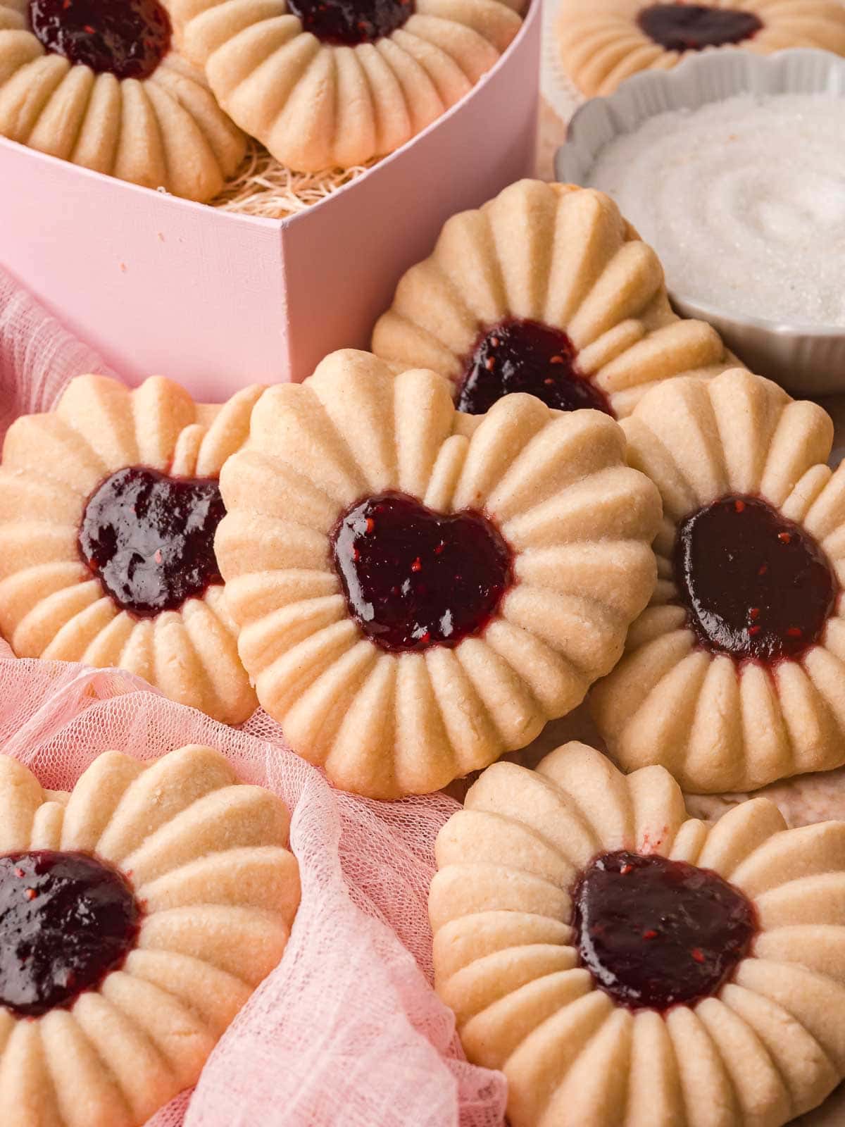 Heart jam cookies displayed together with a pink box and small bowl of jam nearby.