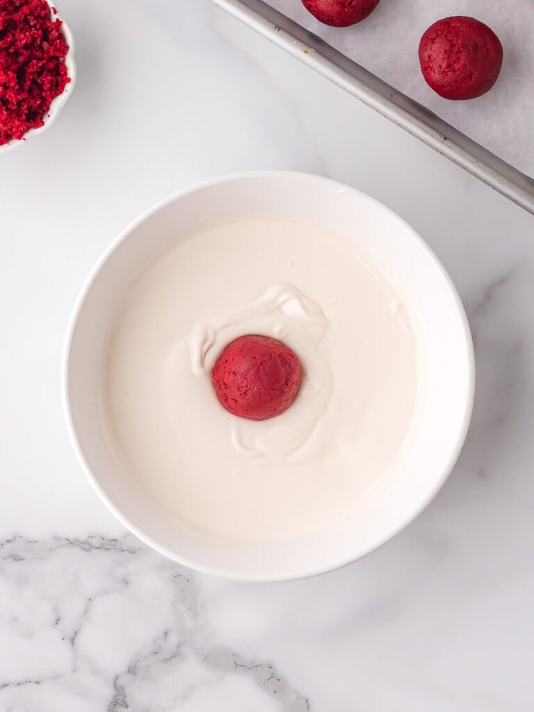 Red velvet truffle center being dipped into melted white chocolate.