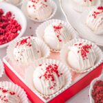 Red velvet truffles arranged in a red gift box with white liners and red velvet crumb topping.