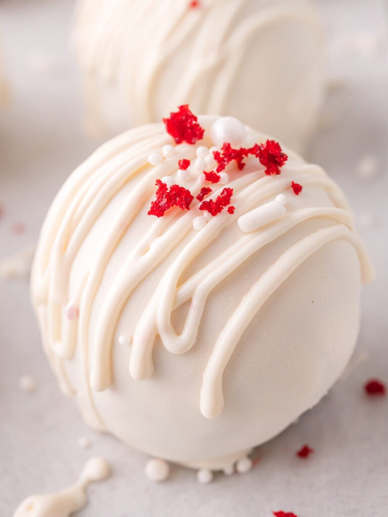 Close-up of a finished red velvet truffle with white chocolate drizzle and red velvet crumbs.