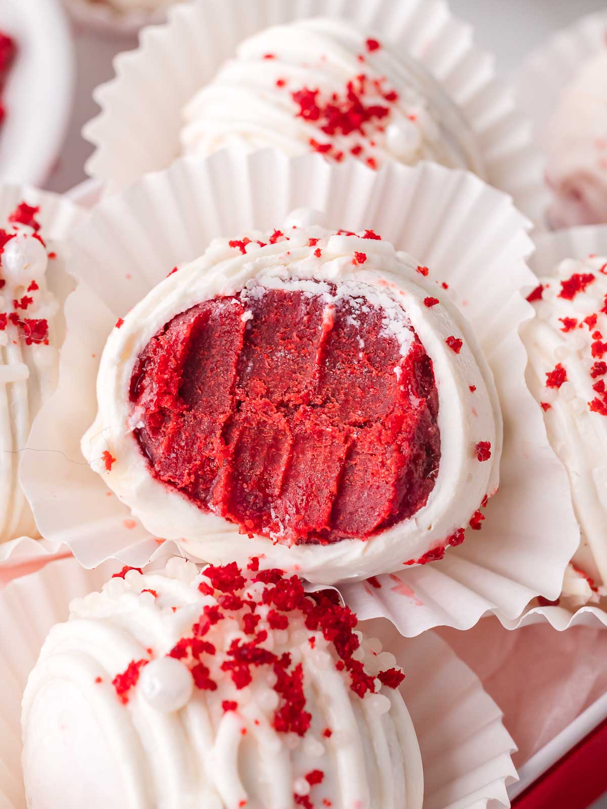 Close-up of a red velvet truffle cut in half showing the creamy red cake center inside white chocolate coating.