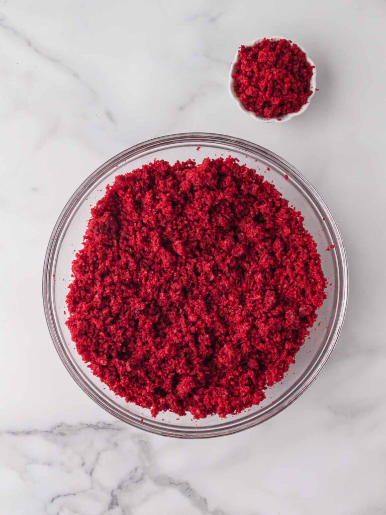Crumbled red velvet cake in a glass mixing bowl with extra crumbs set aside.