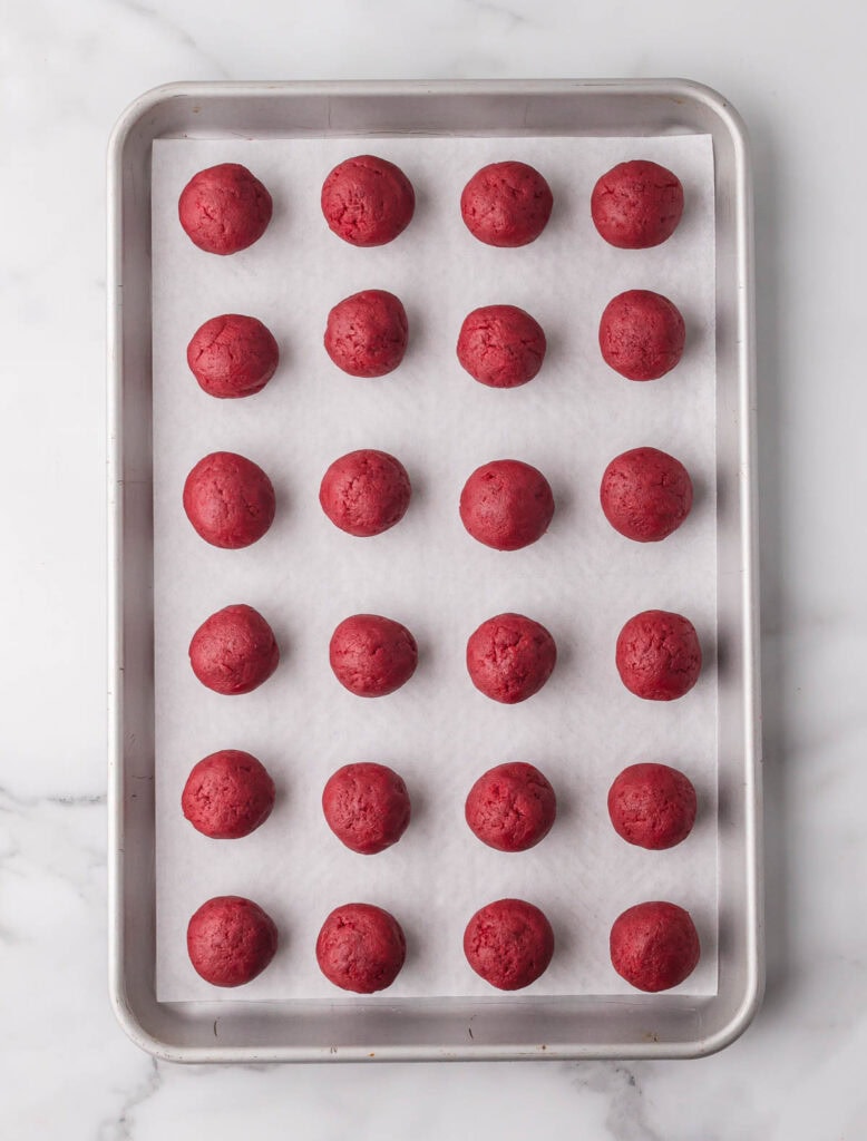 Rolled red velvet truffle centers arranged on a parchment-lined baking sheet.