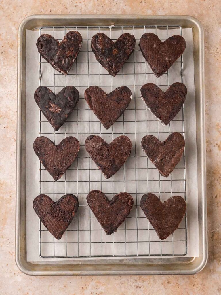Uncoated heart-shaped brownies cooling on a wire rack set over a baking sheet.