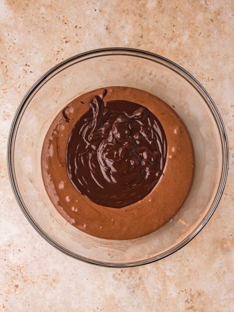 Melted chocolate added to brownie batter in a glass bowl.
