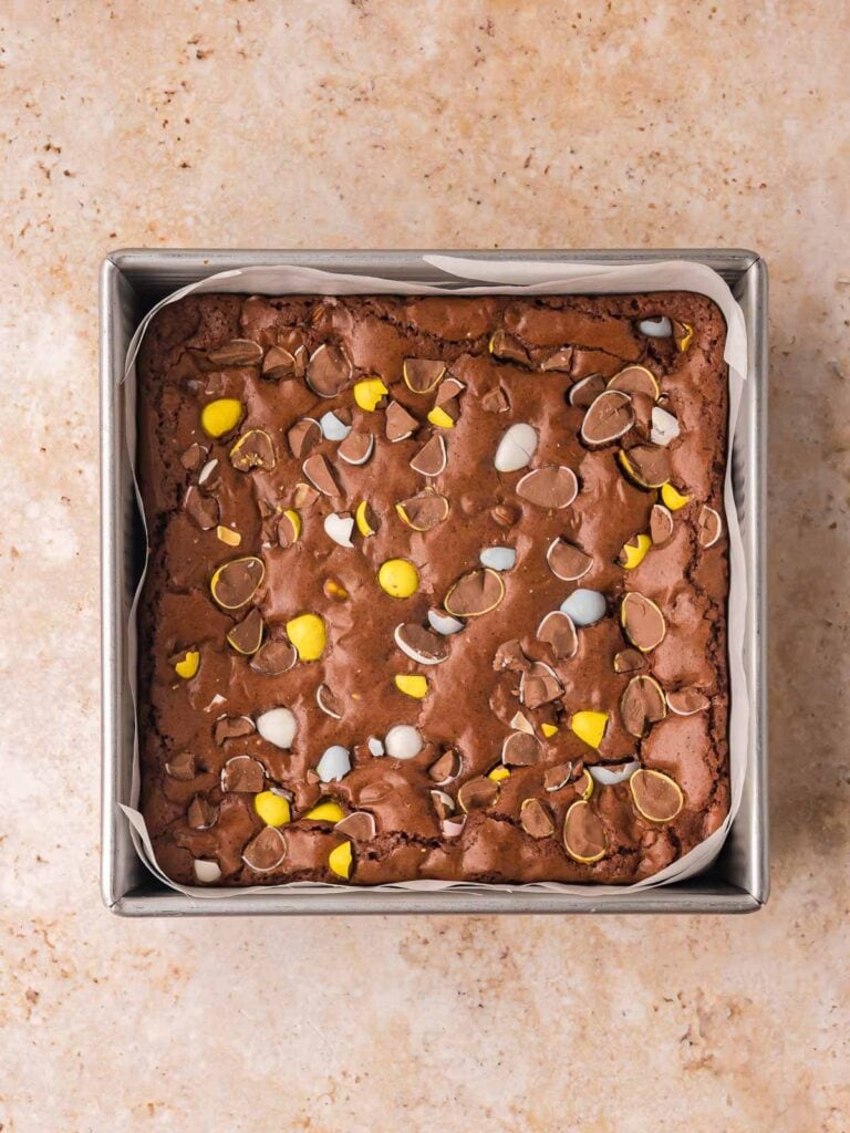 Baked Cadbury egg brownies in a square pan with a crackly top and melted chocolate pieces.